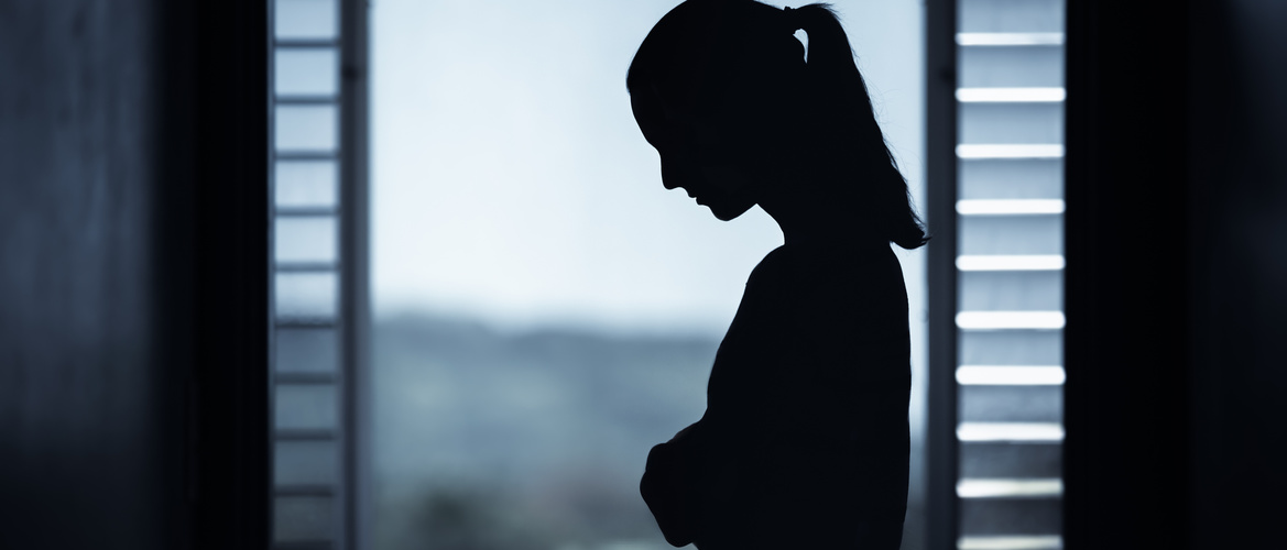 Silhouette of sad woman standing home by the window. Sadness and depressed concept.